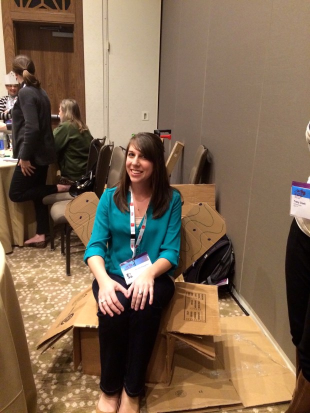 Kristie sitting in the chair we made from cardboard, brads, and nails in 20 minutes in the maker session.